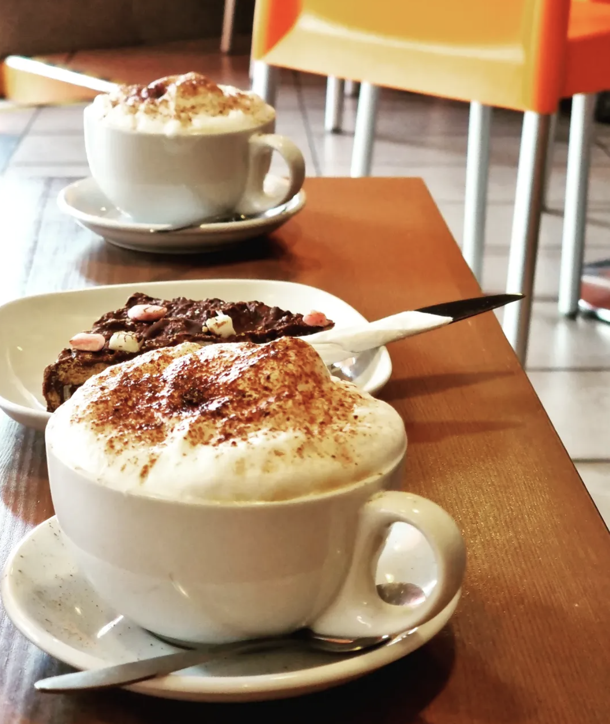 Two cappuccinos topped with cocoa dusted foam, served with a chocolate biscuit at Baobab Cafe
